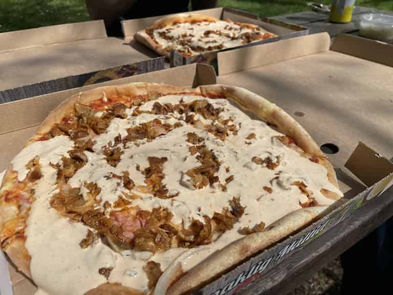 Nahaufnahme von Pizza mit Sahnesoße und gerösteten Zwiebeln, in Pizzakartons serviert.