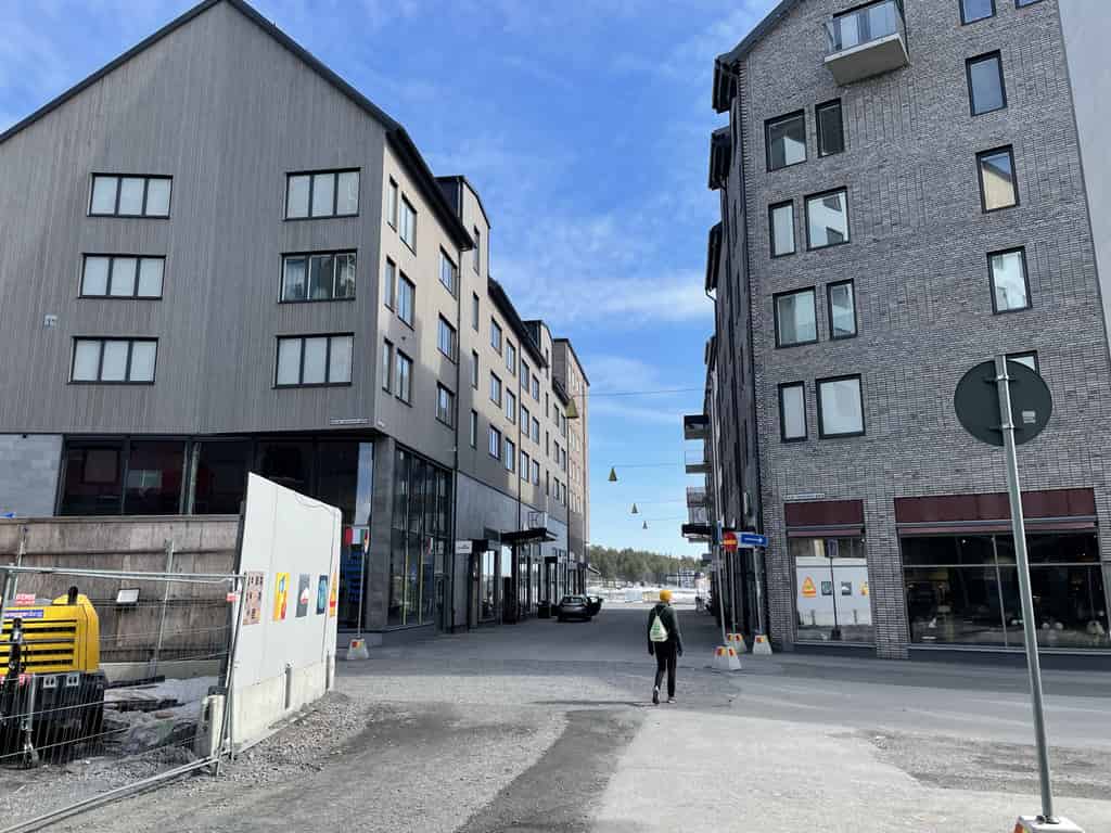 Eine Stadtstraße, gesäumt von modernen Mehrfamilienhäusern mit Geschäften im Erdgeschoss und einer Baustelle an der Seite.
