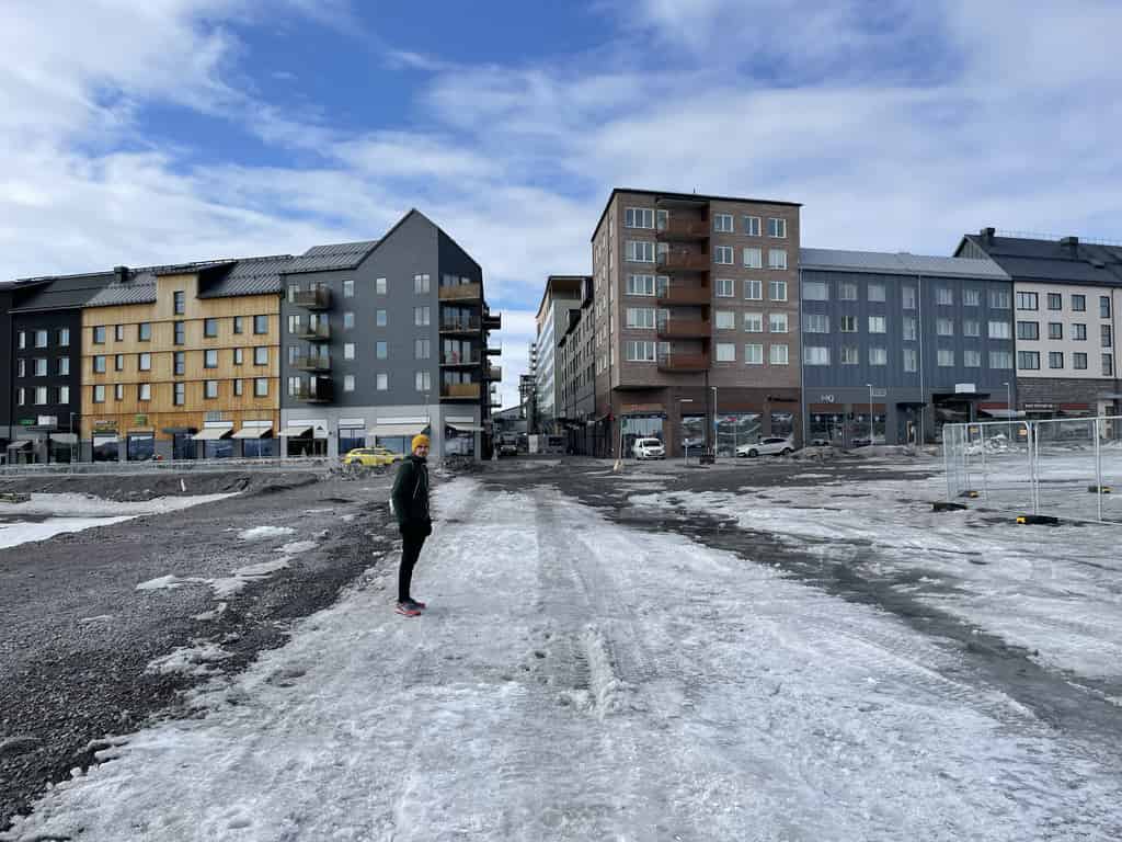 Ein Fußgänger in einer Winterjacke läuft auf einem verschneiten Weg, mit modernen Wohngebäuden im Hintergrund.