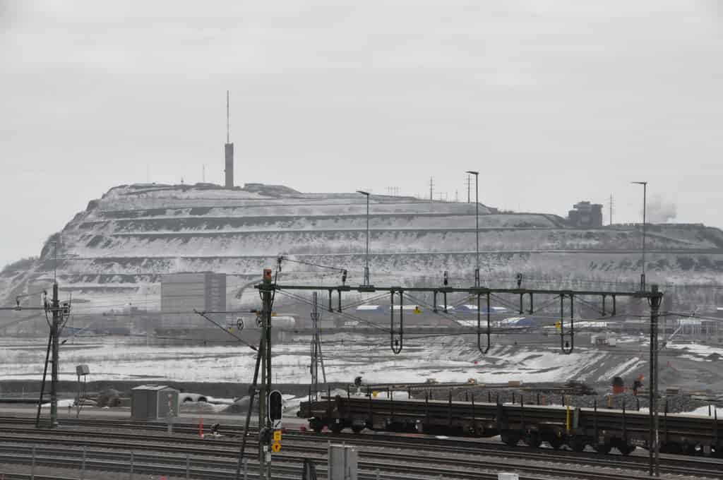Weitblick auf eine verschneite Industrielandschaft mit einem großen Hügel, Bahngleisen und mehreren Industriegebäuden.