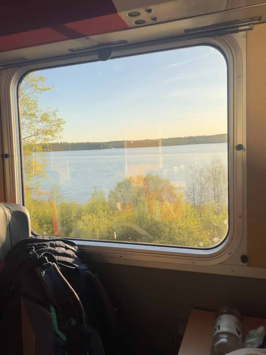 Ein Blick aus dem Fenster eines Zuges auf einen See und Wald bei Sonnenuntergang.