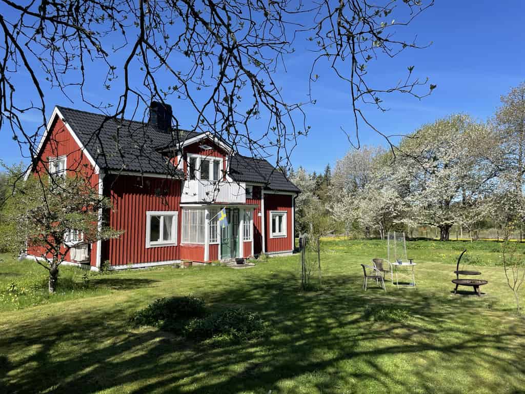 Ein traditionelles rotes schwedisches Haus mit weißer Veranda und blühenden Bäumen im Garten.
