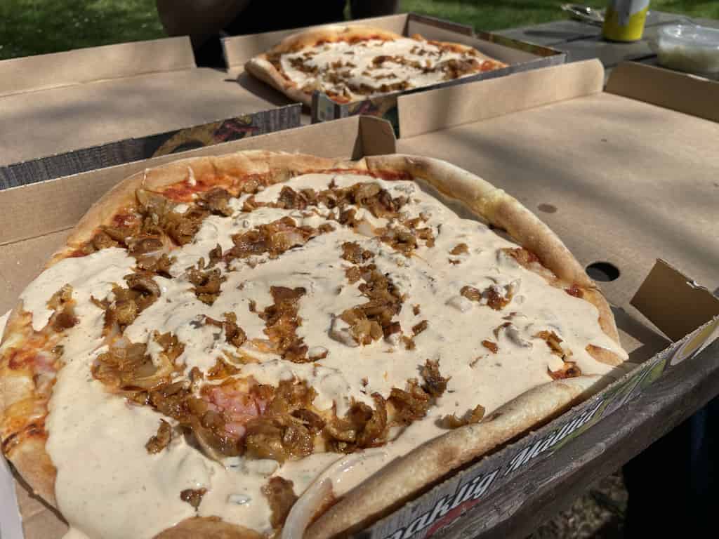 Nahaufnahme von Pizza mit Sahnesoße und gerösteten Zwiebeln, in Pizzakartons serviert.