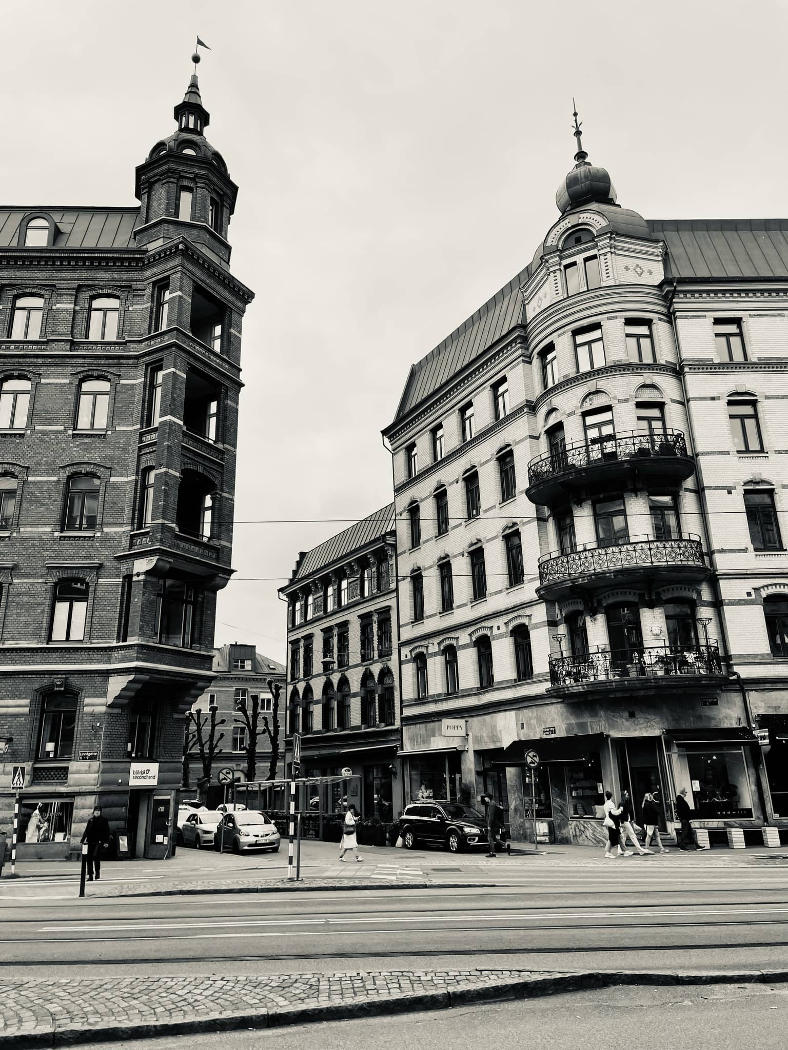 Schwarz-weiß Bild von historischen Gebäuden mit Turm und Kuppel an einer belebten Straßenecke, Personen überqueren die Straße und Autos fahren vorbei.
