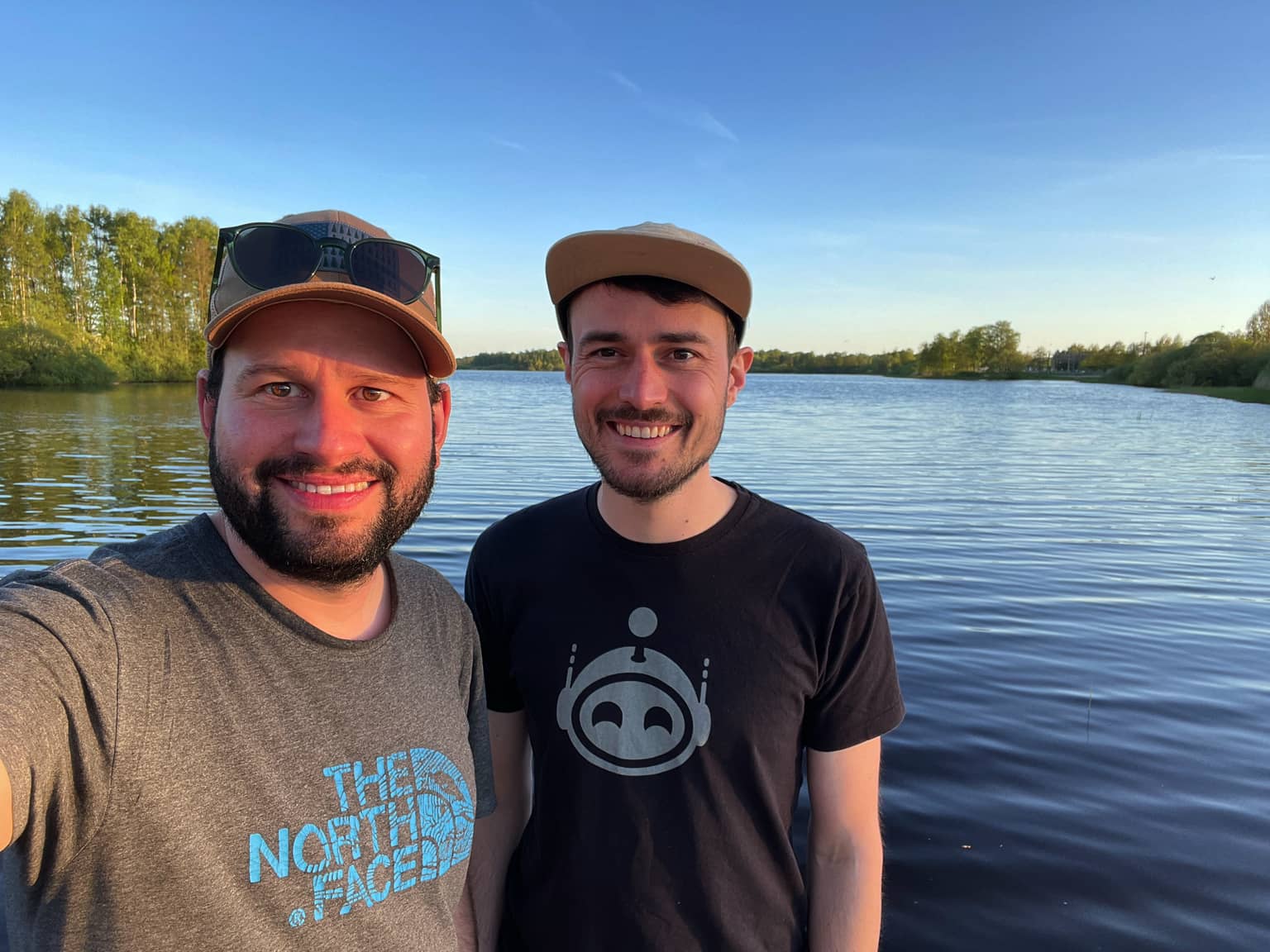Zwei Männer, die vor einem See bei Sonnenuntergang lächeln.