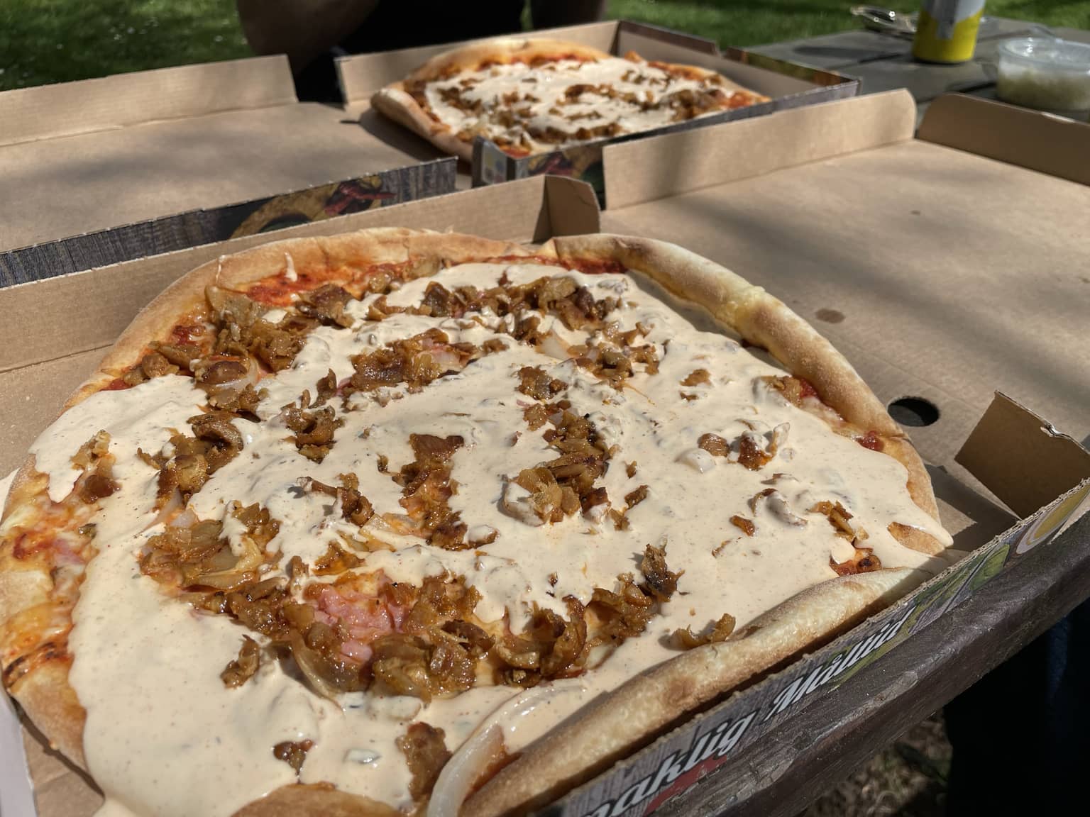 Nahaufnahme von Pizza mit Sahnesoße und gerösteten Zwiebeln, in Pizzakartons serviert.